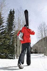 Teenager walking and carrying ski gear.