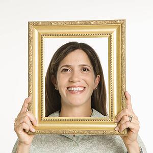 Woman holding frame in front of face smiling.
