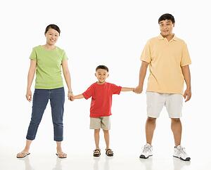 Asian parents holding hands with son in front of white background.