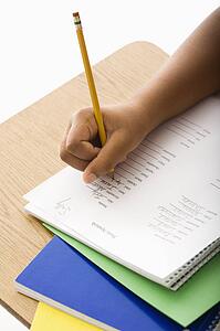Hand of girl at school desk writing in notebook with pencil