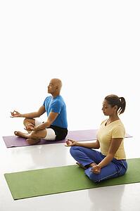 Side view of mid adult man and woman sitting in lotus position on exercise mats with eyes closed and legs crossed.