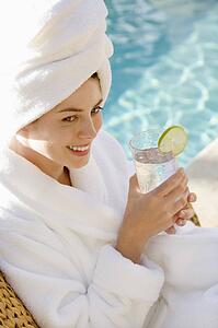 Woman wearing robe and towel on head drinking from glass next to pool