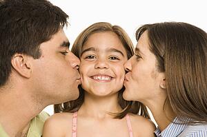 Mother and father kissing smiling daughter