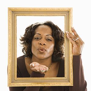 Woman holding frame around head blowing out kiss.