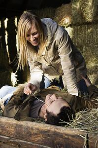 Woman playfully leaning over man lying in hay
