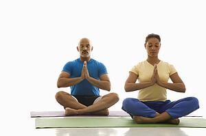 Mid adult man and woman sitting in Namaste position on exercise mats with eyes closed and hands at heart center