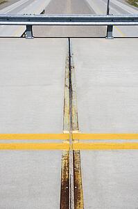 Detail of solid double yellow line in road on overpass with highway below.