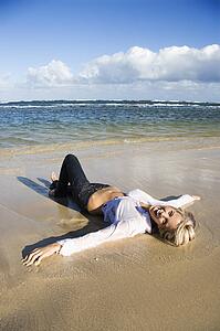 Pretty woman laying on water's edge on beach in Maui, Hawaii smiling
