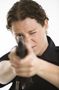 Close up of mid adult female Caucasian law enforcement officer aiming gun at viewer with one eye closed.