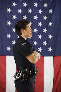 Side view of mid adult Caucasian policewoman standing with arms crossed and American flag as backdrop.