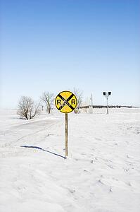Railroad crossing sign in snow covered rural landscape.