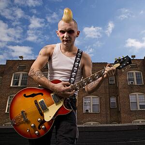 Punk playing guitar with building in background