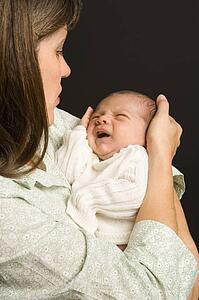 Mother smiling holding baby against black background.
