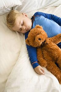 Caucasian toddler boy sleeping in bed with teddy bear.