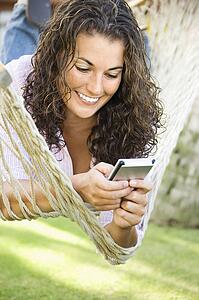 Pretty young adult brunette female laying in hammock using PDA and smiling
