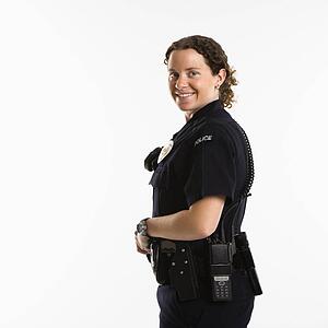 Portrait of mid adult Caucasian policewoman standing with hand on gun holster looking over shoulder at viewer smiling.
