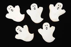 Five sugar cookies in shape of ghosts with decorative icing.