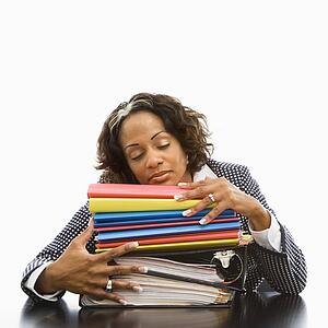 Businesswoman resting head on large stack of books and files with eyes closed
