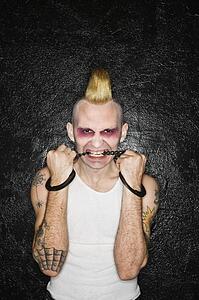 Mid-adult Caucasian male punk biting handcuffs.