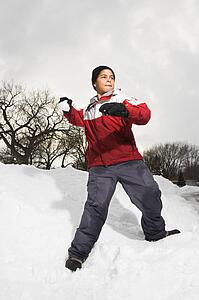 Boy standing in snow throwing snowball.