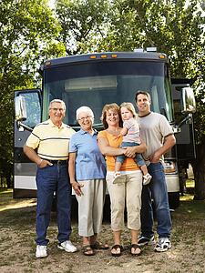 Portrait of three generation Caucasian family standing in front of recreational vehicle smiling and looking at viewer.