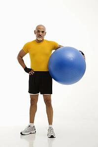 Mid adult multiethnic man standing and holding blue exercise ball looking at viewer.