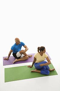 Mid adult man and woman sitting and stretching on exercise mats.