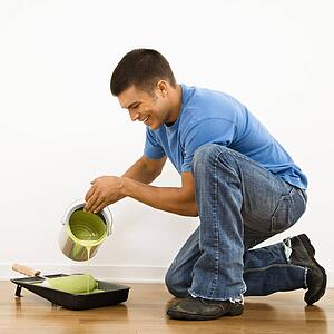 Attractive man smiling and pouring paint into roller pan in home.