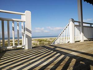 View of beach from porch with railing casting shadow on wooden deck at Bald Head Island, North Carolina