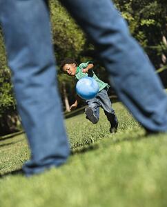Son running and kicking ball towards father in park
