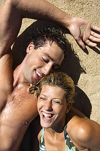 Smiling happy couple lying in sand on Maui, Hawaii beach.