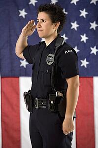 Portrait of mid adult Caucasian policewoman saluting with American flag as backdrop.