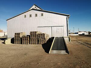 Storage warehouse with ramp and palettes in rural setting.