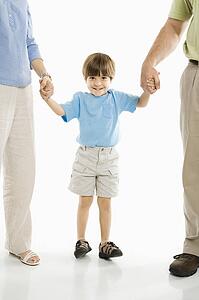 Boy holding hands with parents standing against white background