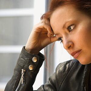 Pretty redhead young woman indoors holding head on hand looking out window