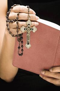 Woman holding Holy Bible open with rosary and crucifix in hand