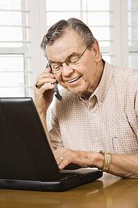 Senior man typing on laptop and talking on cellphone