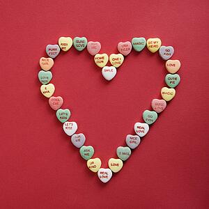 Colorful candy hearts with sayings on them arranged in shape of heart on red background.