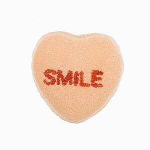 Orange candy heart that reads smile against white background.