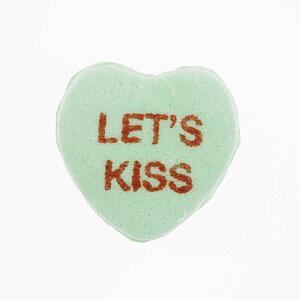 Green candy heart that reads lets kiss against white background.