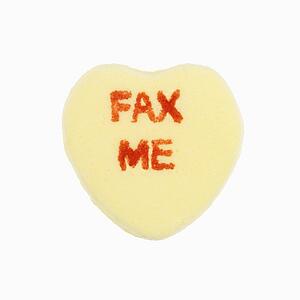 Yellow candy heart that reads fax me against white background.