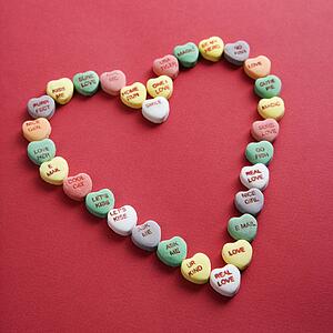 Colorful candy hearts with sayings on them arranged in shape of heart on red background.