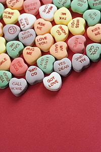 Group of colorful candy hearts with sayings on them arranged on red background.