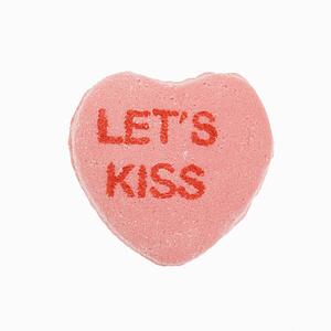 Pink candy heart that reads lets kiss against white background.