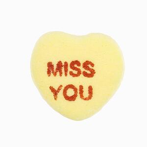 Yellow candy heart that reads miss you against white background.