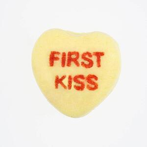 Yellow candy heart that reads first kiss against white background.