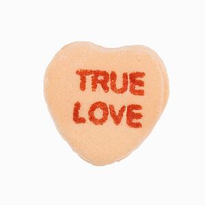 Orange candy heart that reads true love against white background.