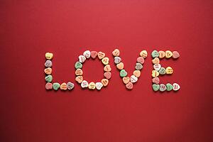 Colorful candy hearts with sayings on them arranged to spell the word love.