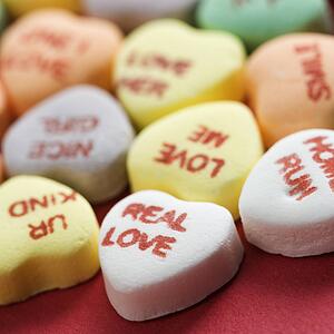 Colorful candy hearts with sayings on them arranged on red background.