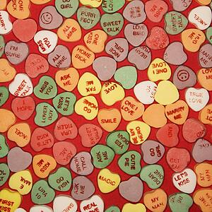 Large group of colorful candy hearts with sayings on them arranged on red background.